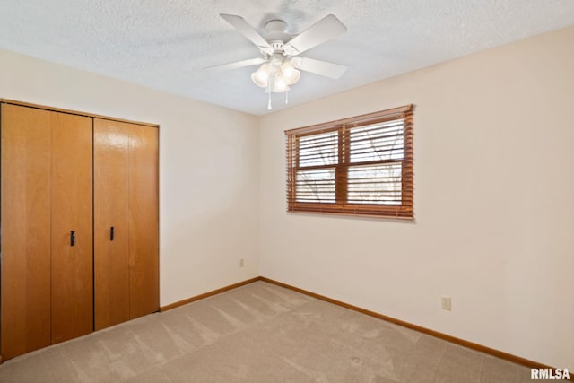 unfurnished bedroom with a closet, light carpet, ceiling fan, a textured ceiling, and baseboards