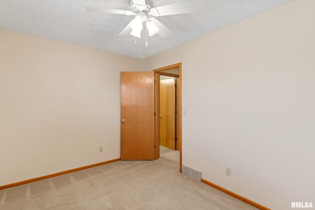 empty room with a textured ceiling, ceiling fan, light colored carpet, visible vents, and baseboards