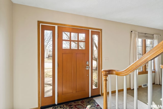 foyer entrance with light tile patterned floors, visible vents, baseboards, and stairs