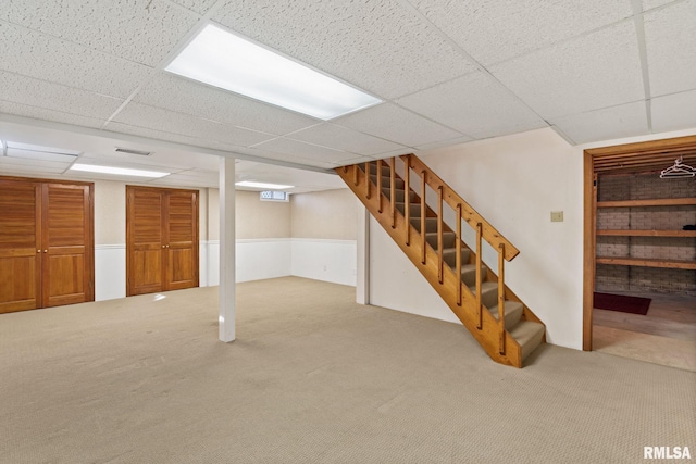 finished basement featuring a paneled ceiling, visible vents, carpet flooring, and stairs