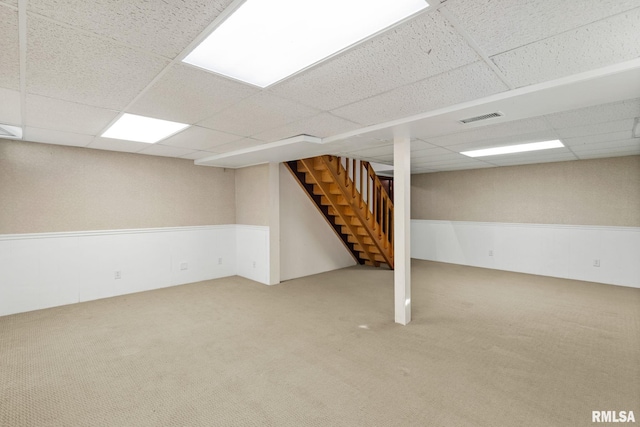 finished below grade area with stairs, a paneled ceiling, carpet flooring, and visible vents