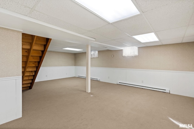 below grade area with carpet, wainscoting, a drop ceiling, and a baseboard radiator