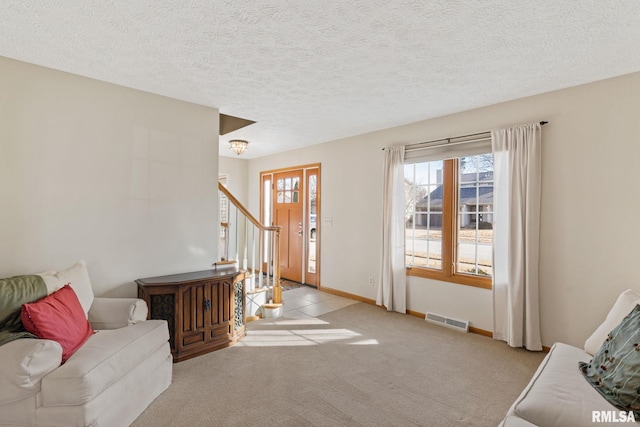 entryway with visible vents, light carpet, a textured ceiling, baseboards, and stairs