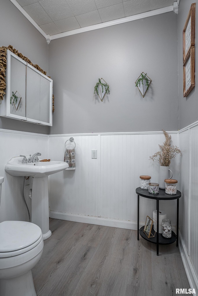 bathroom with ornamental molding, wainscoting, toilet, and wood finished floors