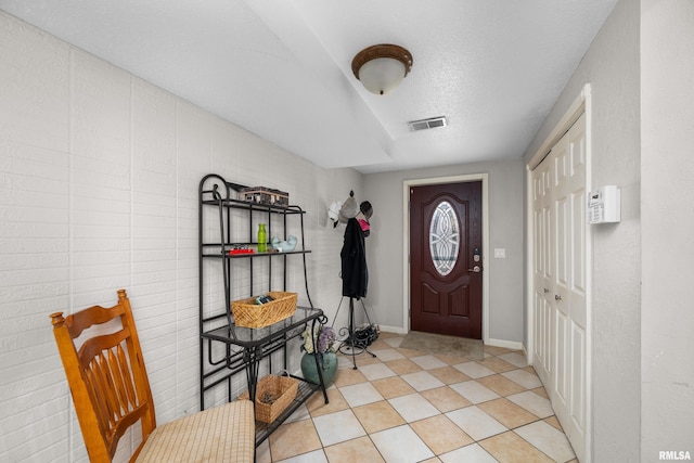 foyer featuring visible vents, a textured ceiling, baseboards, and light tile patterned floors