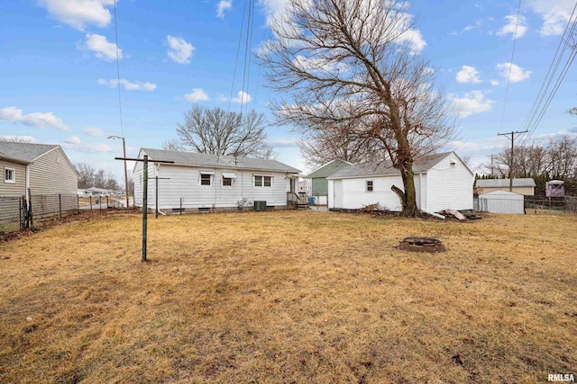 rear view of property featuring a fire pit, a yard, fence, an outdoor structure, and a shed