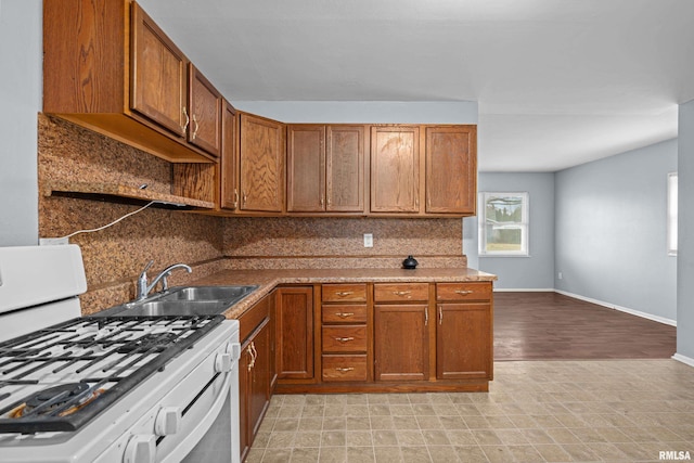 kitchen with brown cabinets, white gas stove, backsplash, a sink, and baseboards