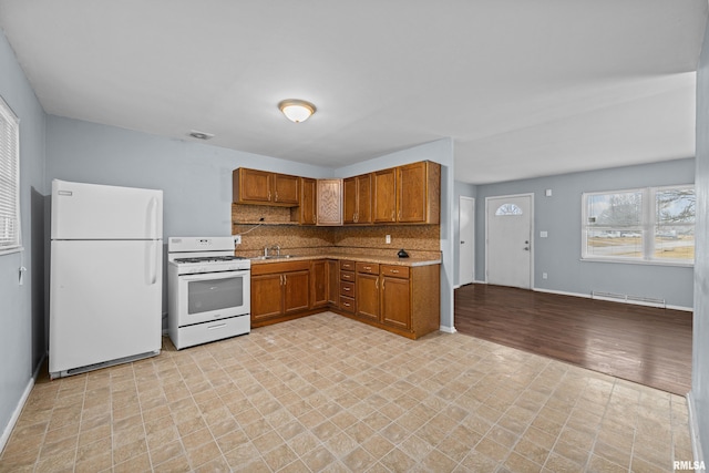 kitchen with white appliances, brown cabinetry, decorative backsplash, light countertops, and a sink