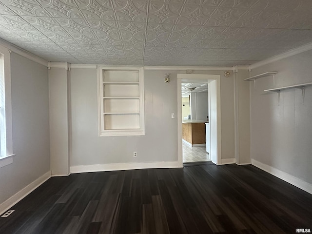 empty room featuring an ornate ceiling, built in shelves, baseboards, and dark wood finished floors