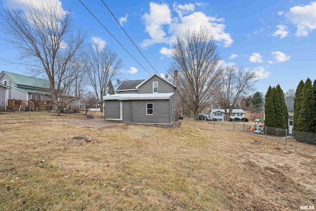 back of house featuring a lawn, a chimney, and fence