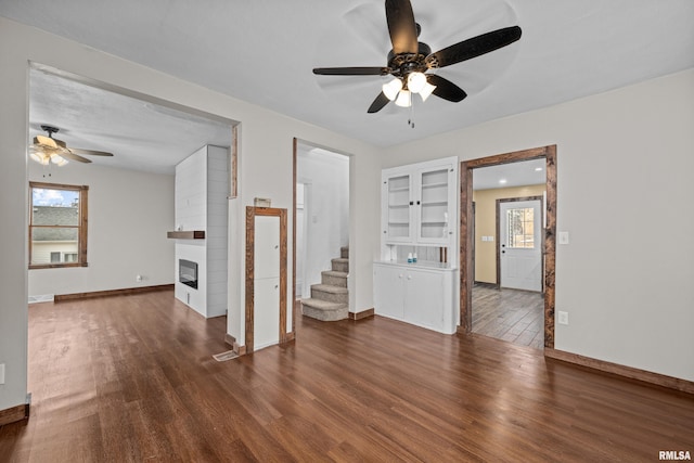 unfurnished living room with a ceiling fan, a fireplace, baseboards, and wood finished floors