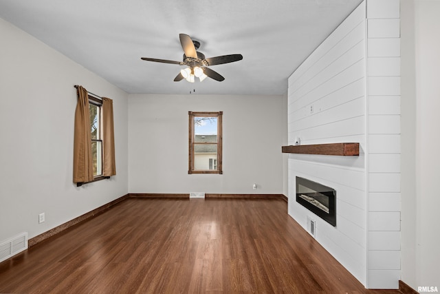 unfurnished living room with dark wood-style flooring, a fireplace, visible vents, a ceiling fan, and baseboards