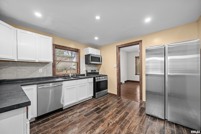 kitchen featuring wood finish floors, dark countertops, decorative backsplash, appliances with stainless steel finishes, and a sink