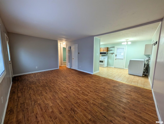 unfurnished living room with washer / clothes dryer, wood finished floors, and baseboards