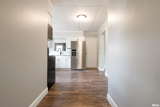 hall with dark wood-style flooring, a drop ceiling, a sink, and baseboards