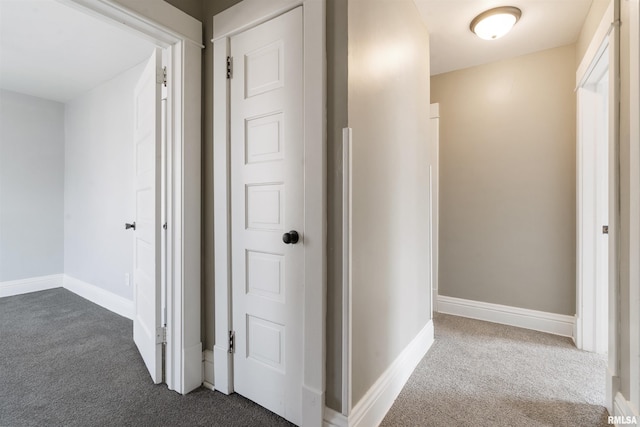 corridor with baseboards and dark carpet