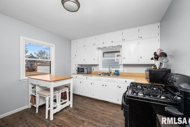 kitchen featuring black gas range oven, stainless steel microwave, dark wood-style flooring, light countertops, and a sink