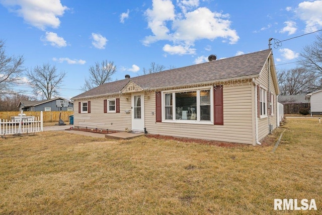 rear view of house with a shingled roof, fence, and a yard