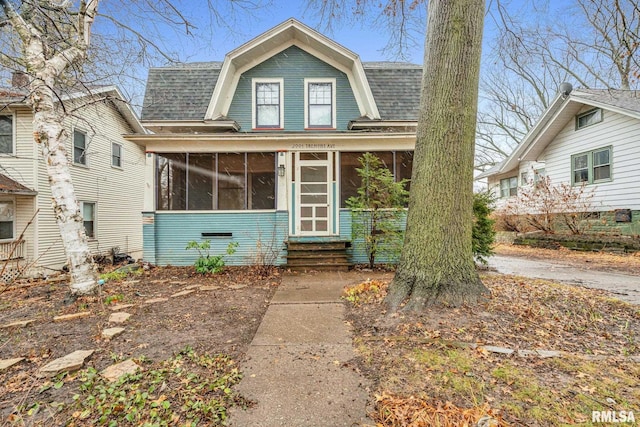 view of front of property with a gambrel roof, a shingled roof, and a sunroom