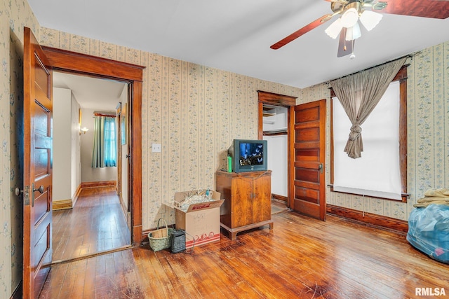 interior space featuring a ceiling fan, hardwood / wood-style flooring, baseboards, and wallpapered walls