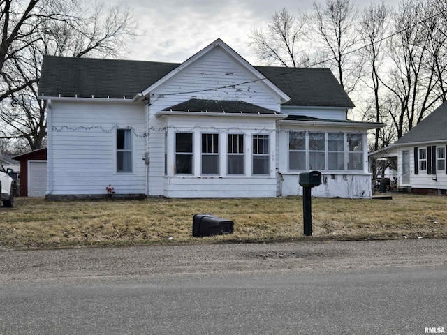 view of front of house featuring a garage, a sunroom, roof with shingles, and a front lawn