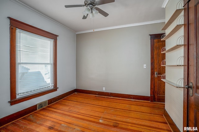 empty room with baseboards, wood finished floors, visible vents, and crown molding