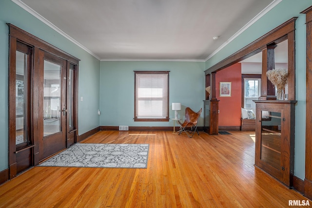 foyer entrance with ornamental molding, wood finished floors, visible vents, and baseboards