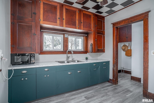 kitchen featuring black microwave, a sink, baseboards, light countertops, and light wood finished floors