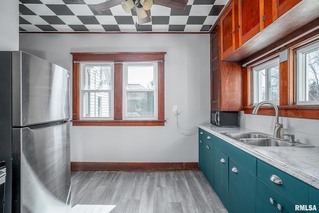 kitchen featuring light countertops, light wood-style flooring, freestanding refrigerator, a sink, and baseboards