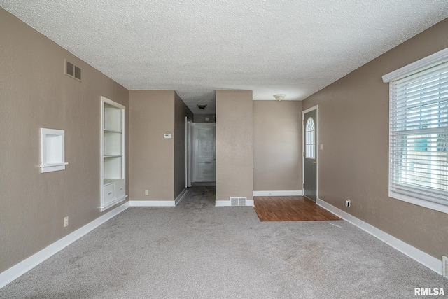 carpeted empty room featuring built in features, baseboards, visible vents, and a textured ceiling