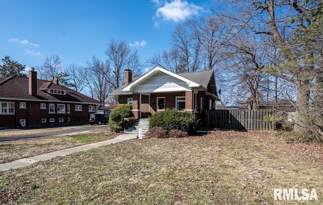 bungalow featuring a front yard, brick siding, and fence