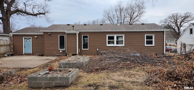 back of property with a shingled roof, a patio area, fence, and a vegetable garden