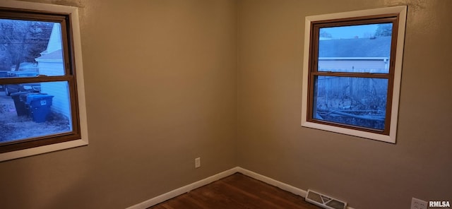 spare room featuring baseboards, visible vents, and dark wood-style flooring