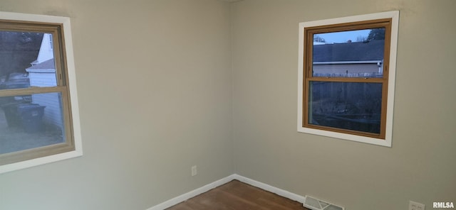 unfurnished room with visible vents, dark wood finished floors, and baseboards