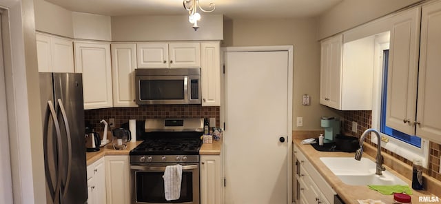 kitchen with stainless steel appliances, light countertops, decorative backsplash, white cabinetry, and a sink