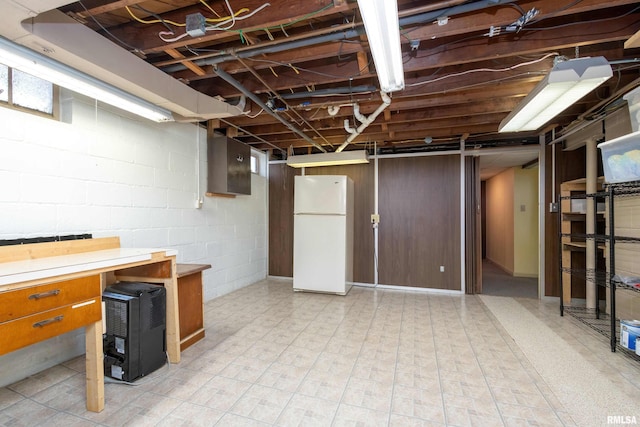 unfinished basement with freestanding refrigerator, concrete block wall, and light floors