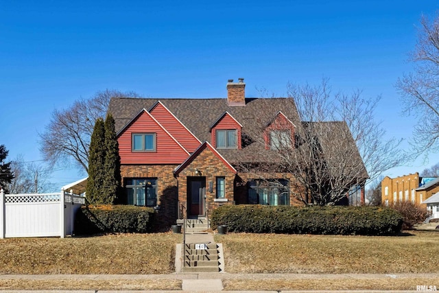 view of front of home featuring stone siding, a shingled roof, a chimney, and fence