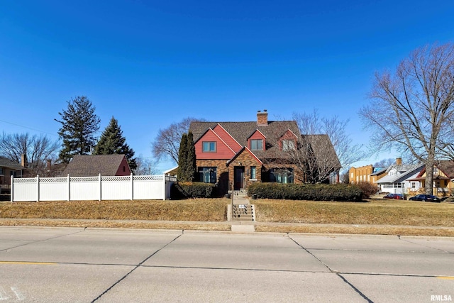 view of front of house featuring stone siding, fence, and a chimney