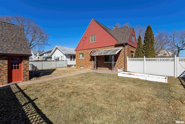 rear view of property with a fenced backyard, a chimney, an outbuilding, a yard, and brick siding