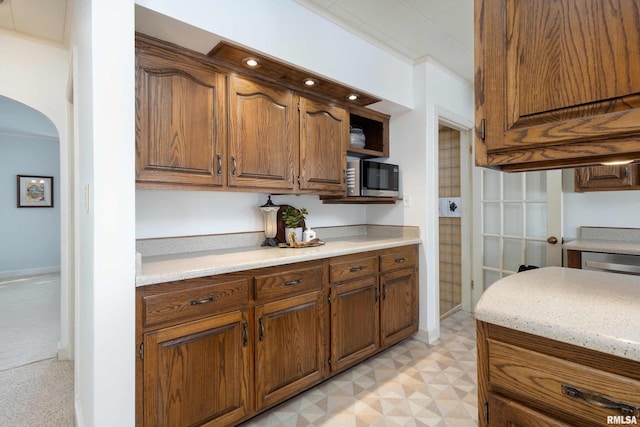 kitchen with light floors, appliances with stainless steel finishes, arched walkways, and brown cabinetry