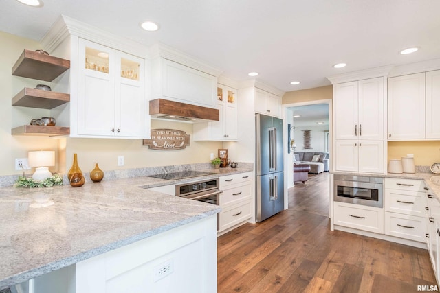 kitchen featuring stainless steel appliances, glass insert cabinets, white cabinetry, wood finished floors, and a peninsula