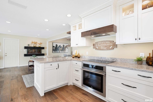 kitchen featuring white cabinets, wood finished floors, oven, a peninsula, and black electric cooktop