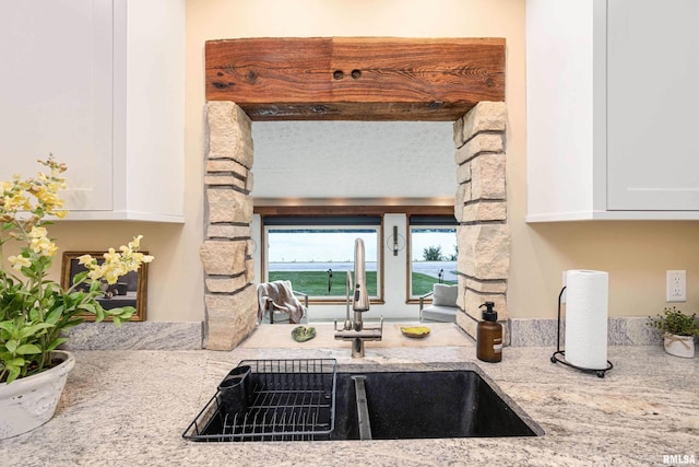 kitchen featuring light stone counters, a sink, and white cabinetry