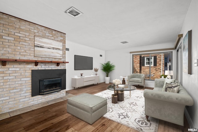 living area featuring a brick fireplace, visible vents, and wood finished floors