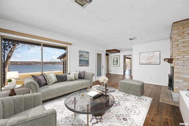 living area featuring hardwood / wood-style floors, a water view, a fireplace, and visible vents