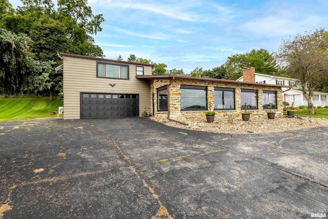 view of front of home featuring stone siding, a chimney, and driveway