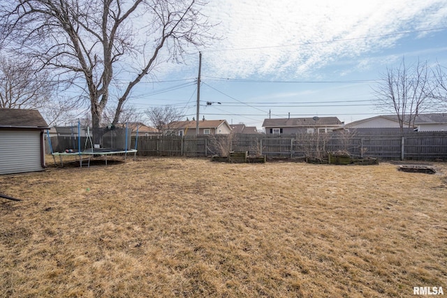 view of yard with a fenced backyard, a trampoline, and an outbuilding