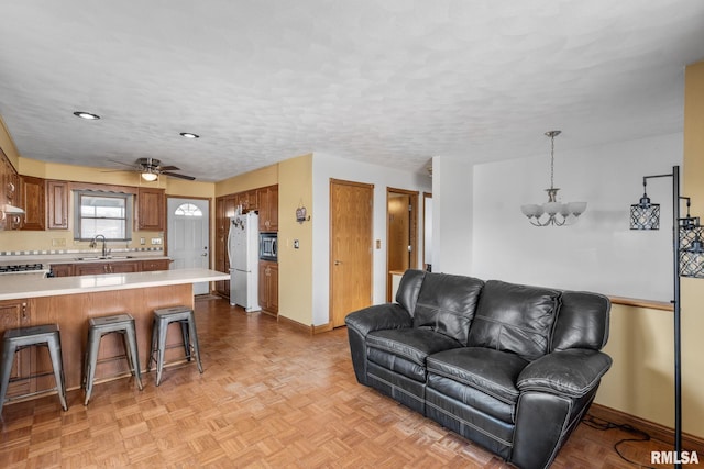 living room with a textured ceiling, ceiling fan with notable chandelier, and baseboards