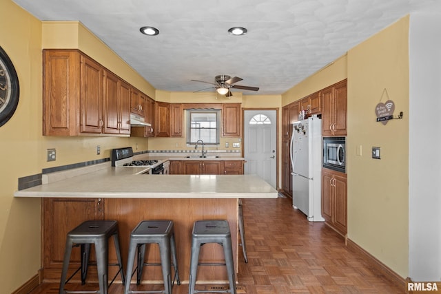 kitchen with white appliances, a peninsula, light countertops, under cabinet range hood, and a sink