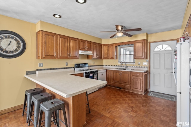 kitchen featuring under cabinet range hood, a peninsula, a sink, gas range gas stove, and a kitchen bar